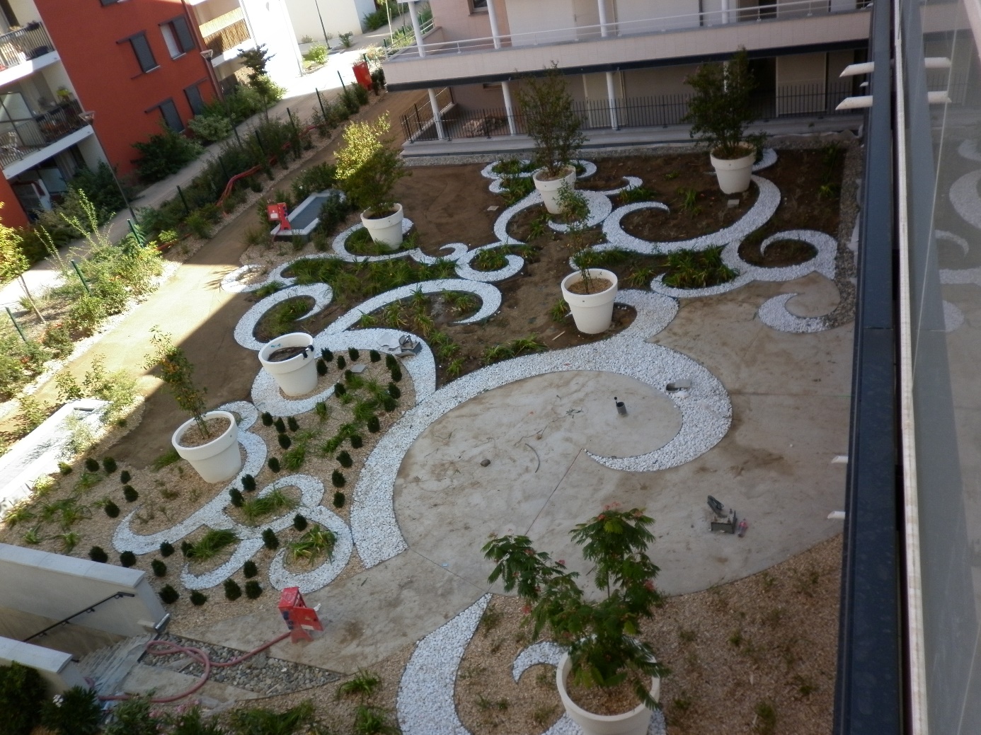 Cour intérieure jardinée avec chemins sinueux et pots de plantes.