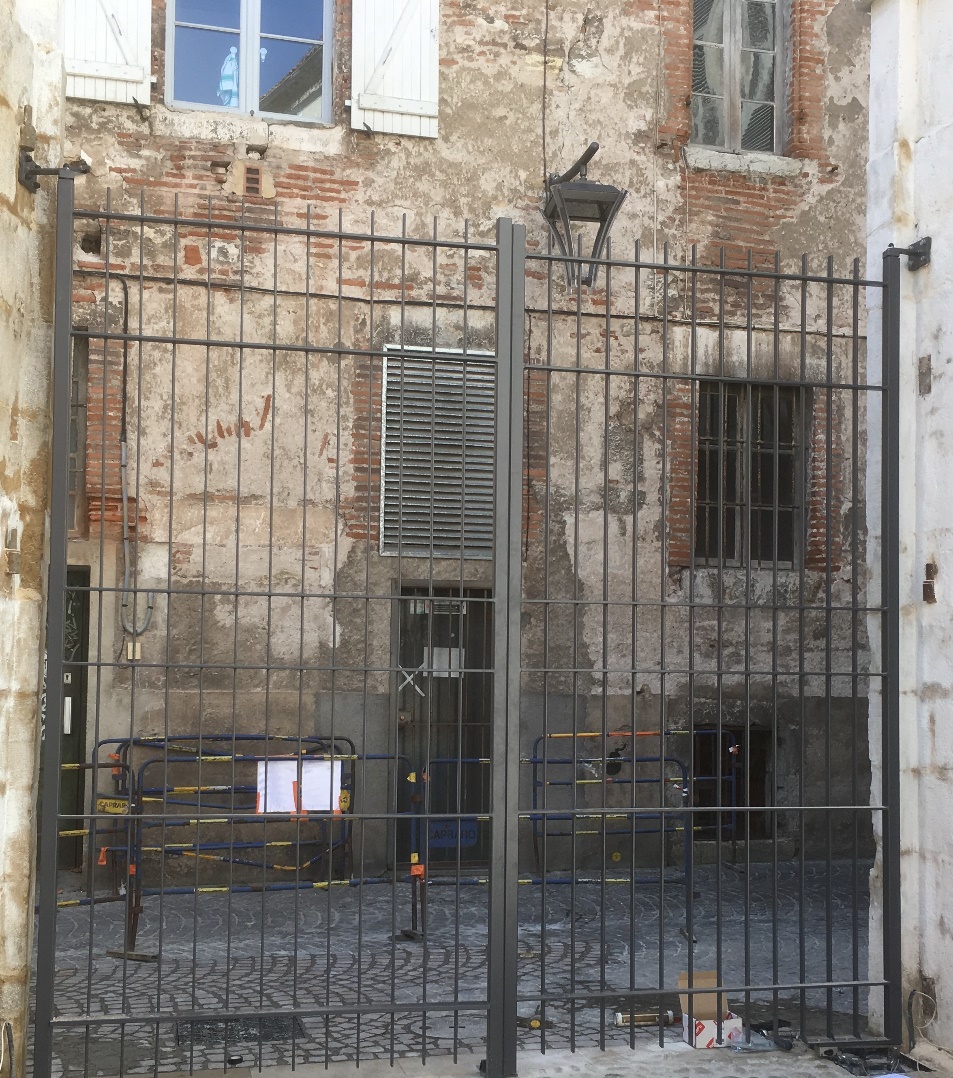Porte en fer forgé devant bâtiment en briques.